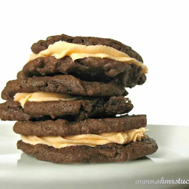 three chocolate filled cookies filled with orange icing stacked on a plate
