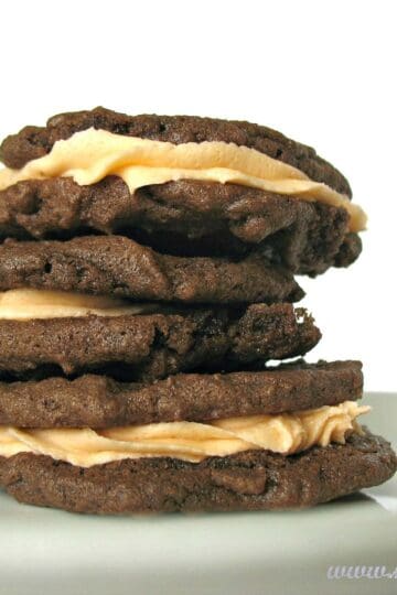 three chocolate filled cookies filled with orange icing stacked on a plate