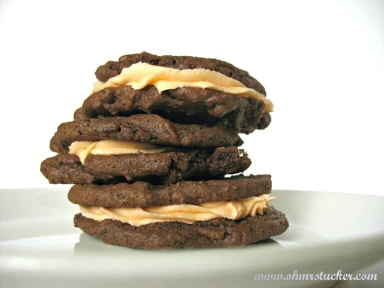 three chocolate filled cookies filled with orange icing stacked on a plate