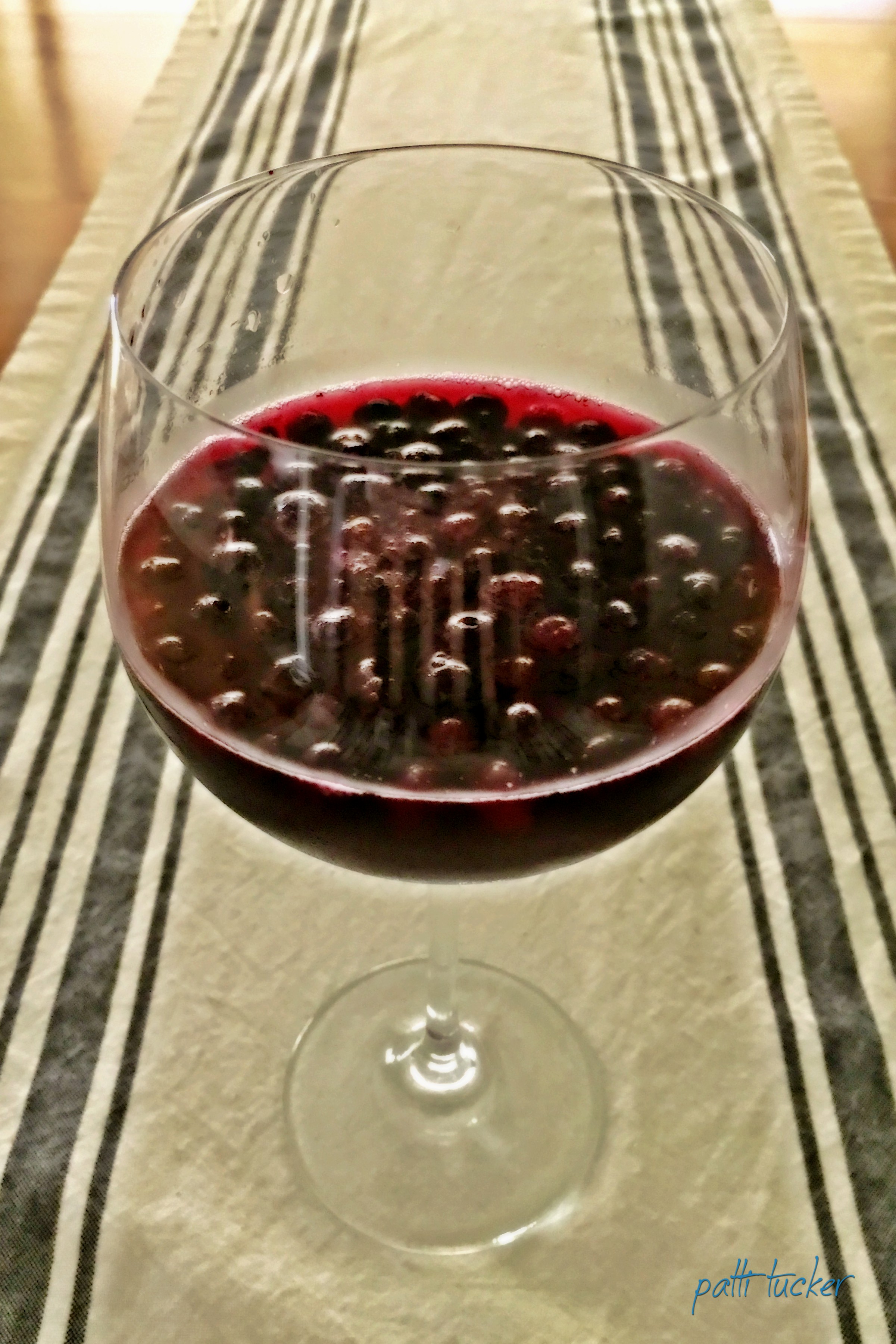 wine glass with wine and blueberries in it on a table