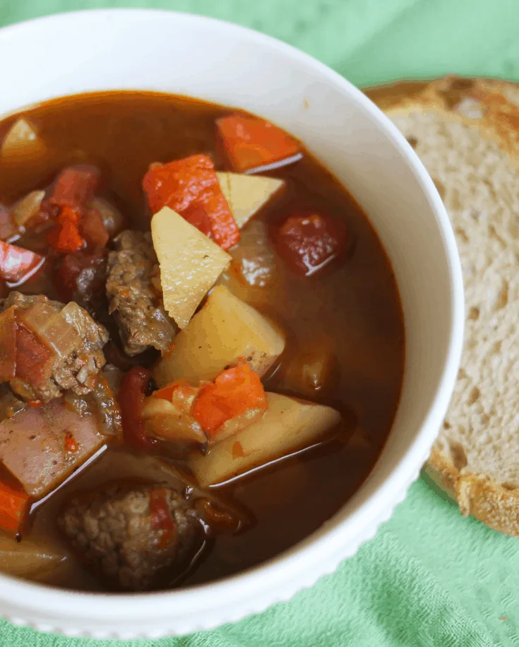 white bowl filled with hungarian goulash with a piece of bread next to it.